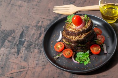 Siyah tabakta ızgara patlıcan, ahşap arka planda izole edilmiş çatal ve zeytinyağı bulunur. Üst manzara, sağlıklı yiyecek kavramı..