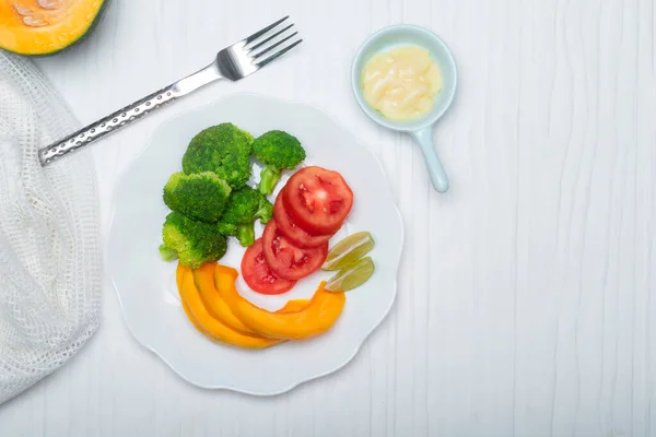 Beyaz tabakta brokoli domates kabağı salatası beyaz ahşap arka planda mayonez var. Yakın plan, üst görüş, sağlıklı yiyecek konsepti..