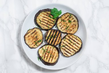 Grilled eggplants in plate isolated on white marble background close up, top view, healthy food concept.