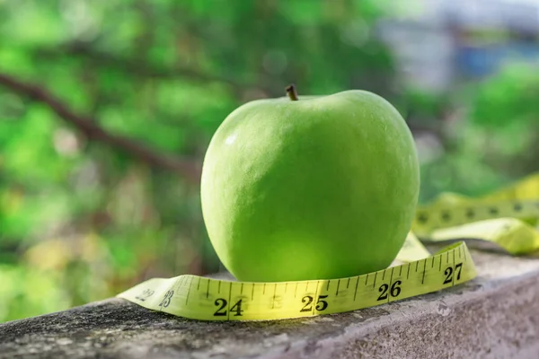 Measure tape and green apple on stone background close up, healthy food concept.