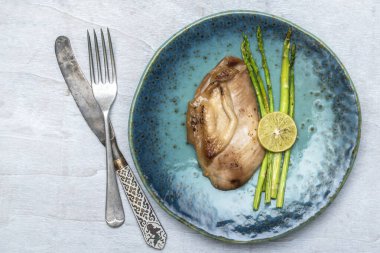 Chicken grill with lemon and asparagus in blue plate on white wood background top view, close up, healthy food concept.
