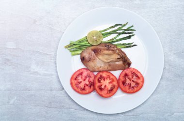 Chicken grill with lemon and asparagus tomato in plate on white wood background top view, close up, healthy food concept.