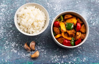 Stir fried chicken add sweet peppers has rice in bowl on blue wood background, top view, food and drink concept.