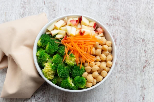 Broccoli salad add apple chickpeas in white bowl isolated on wood background close up, top view, healthy food concept.
