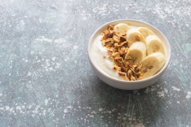 Yogurt in bowl has banana almonds on blue wood background, top view, healthy food concept.