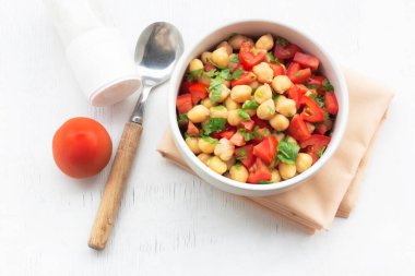 Chickpeas salad add tomato coriander in white bowl isolated on wood background close up, top view, healthy food concept.