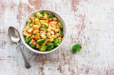 Broccoli salad add apple chickpeas in white bowl isolated on wood background close up, top view, healthy food concept.