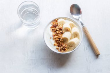 Yogurt in bowl has banana almonds on white wood background, top view, healthy food concept.