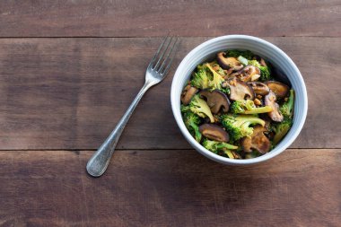 Stir Fried broccoli mushroom in bowl on wood background close up, top view, vegetarian food concept.