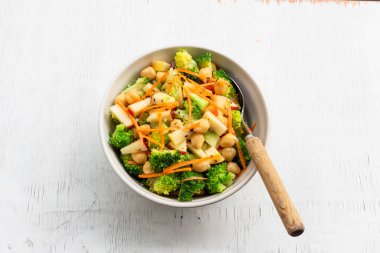 Broccoli salad add apple chickpeas in white bowl isolated on wood background close up, top view, healthy food concept.