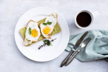 Fried egg on bread avocado spread and coffee on white wood background top view, breakfast food and drink concept.