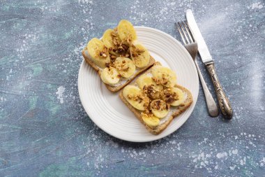 Sandwich open has banana cream cheese almonds and tomato on wood background, top view, copy space, breakfast food concept