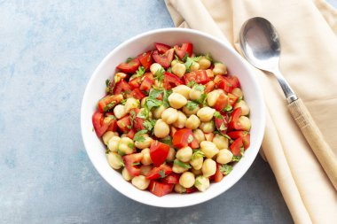 Chickpeas salad add tomato coriander in white bowl isolated on blue wood background close up, top view, healthy food concept.