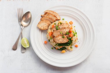 Fried rice dish with chicken breast has vegetable kale carrot in white plate isolated on wood background close up, top view, healthy food and drink concept.