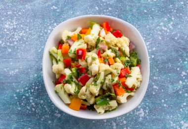 Cauliflower salad in white bowl isolated on blue wood background close up, top view, healthy food concept.