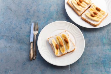 Sandwich open has banana cream cheese almonds on wood background, top view, copy space, breakfast food concept