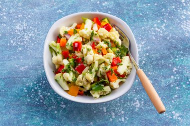 Cauliflower salad in white bowl isolated on blue wood background close up, top view, healthy food concept.