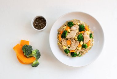 Tavuk göğsü ile kızartılmış pirinç tabağında beyaz ahşap arka planda izole edilmiş sebze brokoli kabağı bulunur. Üst manzara, sağlıklı yiyecek ve içecek konsepti..