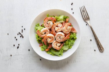 Shrimp salad lettuce carrot tomato in bowl on wood background top view, healthy food concept.