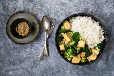 Kızarmış brokolili tofu fıstığı. Siyah kasede kahverengi pirinç var. Arka planda, üst tarafta, vejetaryen sağlıklı yiyecek konsepti..