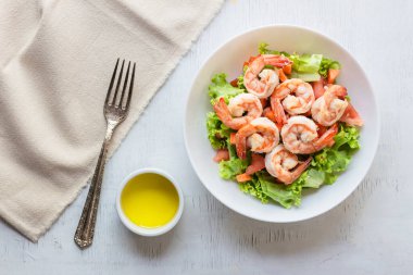 Shrimp salad lettuce carrot tomato in bowl on wood background top view, healthy food concept.
