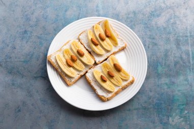 Sandwich open has banana cream cheese almonds on wood background, top view, copy space, breakfast food concept.
