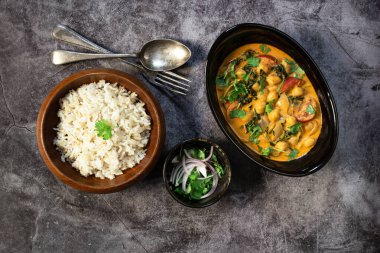 Chickpea curry with spinach has brown rice on black stale background, top view, healthy vegan food concept. clipart