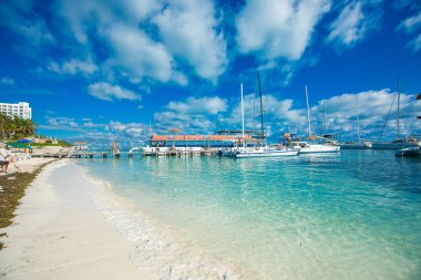 Cancun Hotel Zone 'daki Playa Tortugas manzarasında turkuaz suları, yumuşak beyaz kumlar ve yakınlardaki marinaya demir atmış katamaranlar görülüyor. Bu popüler plaj, canlı tropikal atmosferi, Isla Mujeres feribot ulaşımı ve canlı su fro ile bilinir.