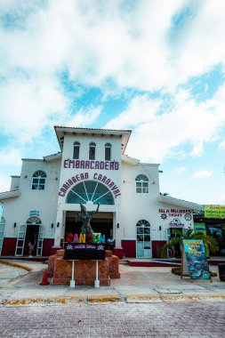 Cancun Otel Bölgesi 'ndeki Playa Tortugas' ın giriş ve otoparkının fotoğrafı Embarcadero binasını, arabaları ve yakındaki tatil köylerini gösteriyor. Burası Isla Mujeres feribotları ve plaj kulüplerine erişimi olan önemli bir ulaşım noktası olarak hizmet vermektedir. Th