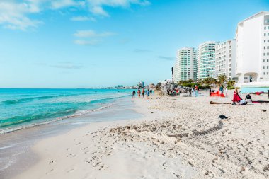 Cancun Otel Bölgesi 'ndeki Playa Chacmool' da bir plaj fotoğraf çekimi görüntüsü. Kırmızı bir kumaş, doğal kayalık uçurumlar ve sahil manzaralı oteller ve turkuaz sulara karşı bir dekor olarak kullanılır. Sahne sanatsal yaratıcılığın bir anını yakalıyor.