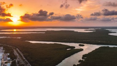 Büyük bir su kütlesinin üzerinde güzel bir günbatımı. Gökyüzü bulutlarla dolu ve güneş uzaklardan batıyor. Su çok sakin. Cancun Otel bölgesinin havadan görünüşü, Quintana Roo Mexico 