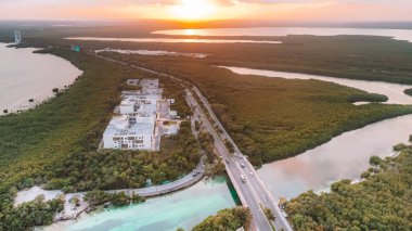 Nehrin üzerinde köprüsü ve arka planda büyük bir binası olan güzel bir manzara. Gökyüzü turuncu ve güneş batıyor. Cancun Otel bölgesinin havadan görünüşü, Quintana Roo Mexico