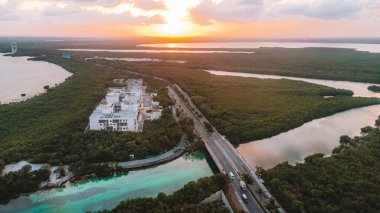 Nehrin üzerinde köprüsü ve arka planda büyük bir binası olan güzel bir manzara. Gökyüzü turuncu ve güneş batıyor. Cancun Otel bölgesinin havadan görünüşü, Quintana Roo Mexico