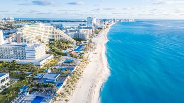 Mavi okyanusu ve arka planda birkaç binası olan güzel bir sahil. Kumsal boş ve gökyüzü bulutlu. Cancun Otel bölgesinin havadan görünüşü, Quintana Roo Mexico