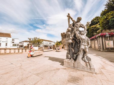 Kilkenny Ireland, Temmuz 2023 Bir erkek ve bir kadın heykeli bir binanın önündeki kaldırımda. Heykel birkaç bankla çevrili ve birkaç kişi onların üzerinde oturuyor. Kilkenny, İrlanda heykeliyle manzara huzurlu ve sessiz.