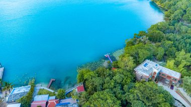 Bacalar, Mexico, Quintana Roo, Beautiful blue lake with a house on the shore. The house is surrounded by trees and there are boats docked in the water