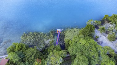 Bacalar, Mexico, Quintana Roo, Beautiful blue lake with a dock and trees in the background. The water is calm and clear, and the dock is red. The trees are lush and green, and the overall mood of the image is peaceful and serene