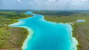 Bacalar, Mexico, Quintana Roo, Beautiful blue river with trees and grass on the banks. The water is calm and clear. The sky is blue and there are no clouds