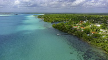 Bacalar, Mexico, Quintana Roo, Beautiful blue ocean with a dock and houses in the background. The water is calm and the sky is cloudy