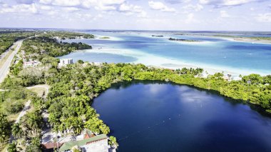 Bacalar, Mexico, Quintana Roo, Beautiful lake surrounded by trees and houses. The lake is blue and calm. The trees are green and lush. The houses are small and scattered around the lake