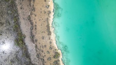 Bacalar, Mexico, Quintana Roo, Beautiful blue ocean with a sandy beach. The water is calm and the shoreline is lined with rocks. The sky is clear and the sun is shining brightly, creating a serene and peaceful atmosphere