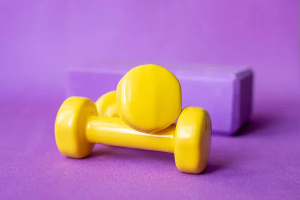 Two small yellow dumbbells on a lilac sports mat. Front view. Place for text. Sport extends life. Selective focus on dumbbells