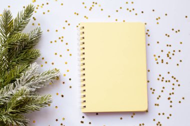 Sarı boş not defteri altın parıltılı beyaz bir Noel arkaplanındaki spirallerde. Yukarıdan bak. Mesajın için yer aç. Yeni yıl için ideal