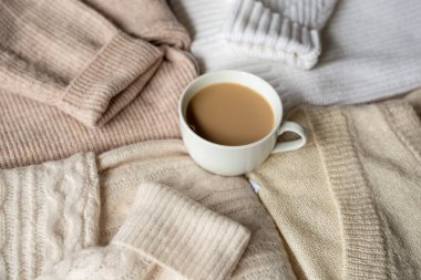 Bej örülmüş kazakların arasında beyaz bir fincan kakao. Sonbahar havası, kızlık zarı, sıcaklık ve konfor