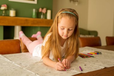 Easter and the child. Development, drawing. Cute cute girl with blond hair paints an Easter picture lying on the table in a bright interior