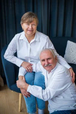 Emekli, mutlu bir evlilik, aşk. Yaşlı bir çift kanepede sarılıyor. Mavi ve beyaz renkli fotoğraf