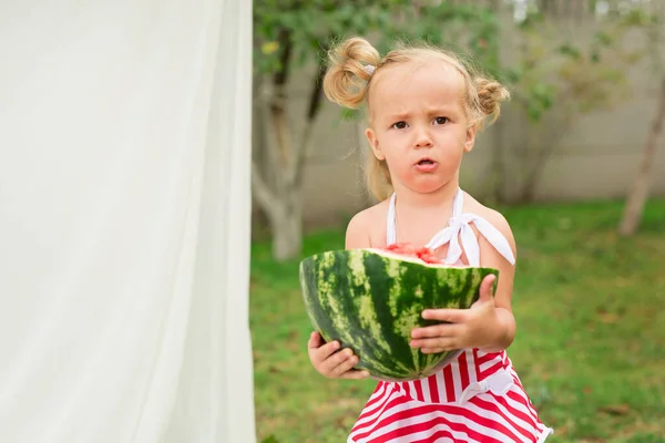 Yaz, çocuklar, vitaminler. Çizgili beyaz ve kırmızı mayo giymiş, beyaz arka planda beyaz bir yatakta büyük olgun bir karpuz taşıyan iki kuyruklu tatlı kız..