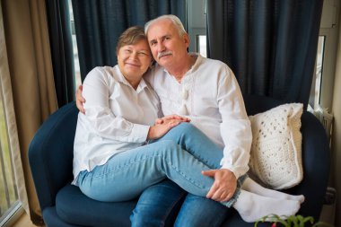 Emekli, mutlu bir evlilik, aşk. Yaşlı bir çift kanepede sarılıyor. Mavi ve beyaz renkli fotoğraf