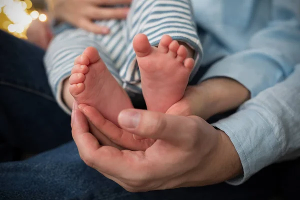 stock image Paternity. Childhood. Family. Caring parents hands hold the little childs feet. Blue family outfit