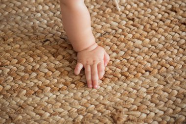 Sürünen, çocuk gelişimi, bebeğim. Bir çocuk, bej renkli, saman bir halıda el ele tutuşur..